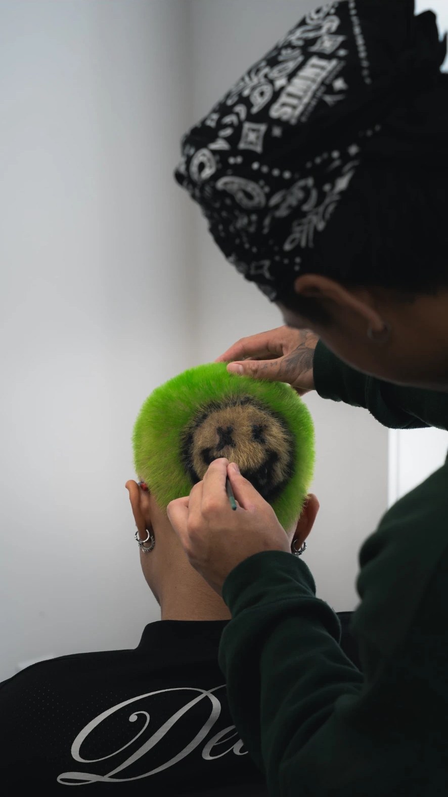 Artist freehand-painting a smiley design into bright green hair colour at fyf North